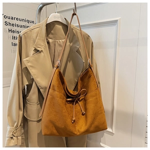 Detail of tan suede tote bag with drawstring bow on a minimalist stylish coat