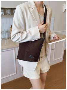 Détail d'un sac bandoulière en daim marron foncé avec texture mate et logo