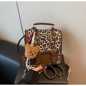 Detail of leopard print flap backpack featuring vintage metal buckles and plush bear charm