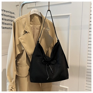 Detail of a black canvas hobo tote bag with a ribbon bow on a khaki trench coat background