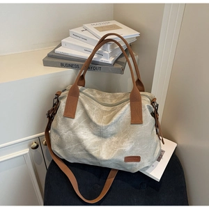 Detail of canvas tote bag with brown woven straps and logo on washed texture fabric