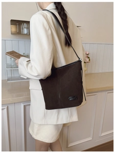 Détail du sac à bandoulière en daim marron foncé avec lanière en cuir noir et logo
