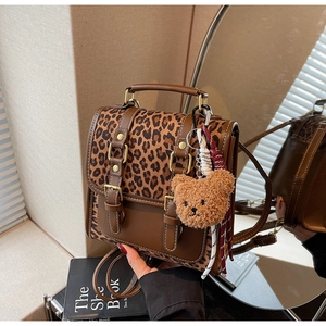 Detail of leopard print backpack with brown leather accents and plush bear charm