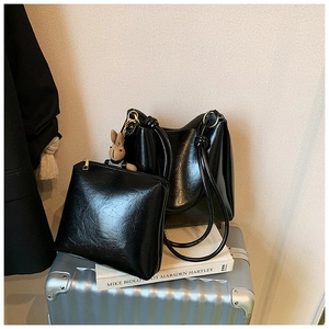 Close-up of black oil wax leather tote set with knot handles and rabbit charm on suitcase