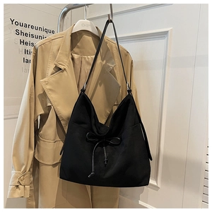 Detail of black tote bag with bow drawstring hanging next to a beige trench coat