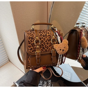 Detail of vintage leopard print backpack with brown leather straps and plush bear charm