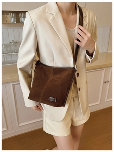 Sac seau en daim marron avec bandoulière en cuir et logo porté sur un tailleur beige