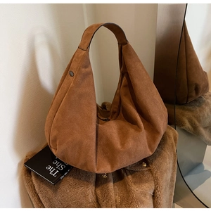 Détail macro de la texture en daim marron caramel sur un sac hobo vintage à l'épaule