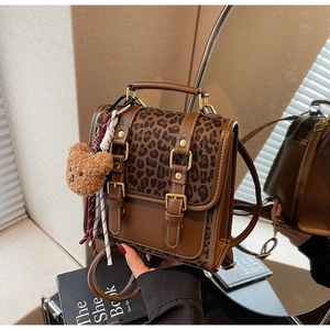 Detail of leopard print backpack with brown trim, gold buckles and plush bear charm