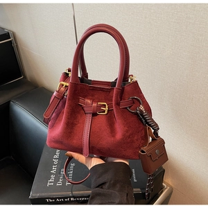 Detail of burgundy faux suede bucket bag with leather handles and a side mini pouch