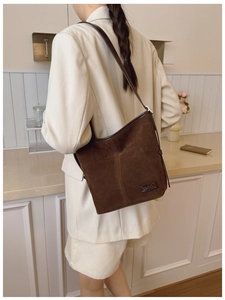 Sac seau en daim marron porté par un mannequin dans une cuisine au design épuré