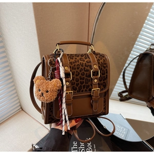 Detail of retro leopard print backpack featuring metal buckle and plush bear charm decoration