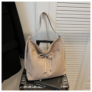 Close-up of beige suede shoulder bag with decorative bow tie on a metal suitcase