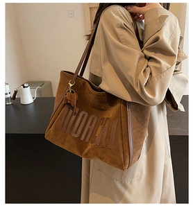 Close-up of brown suede tote bag featuring embossed logo detail and leather strap