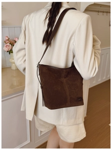 Détail d'un sac seau en daim marron avec plaque logo en métal sur un blazer blanc