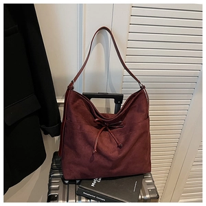 Detail of burgundy suede tote bag with bow drawstring and side pockets on a suitcase
