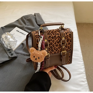 Detail of leopard print backpack with brown trim, metal buckle, and plush bear charm
