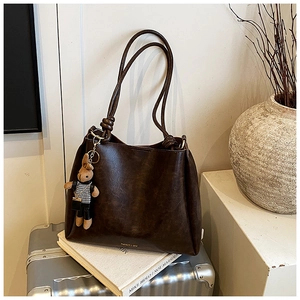Detail of dark brown faux leather tote bag with a cute plaid rabbit charm on an aluminum suitcase