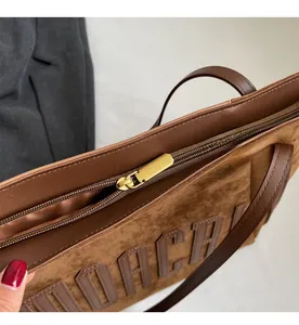 Detail view of the smooth metallic gold zipper on a large dark brown suede tote bag