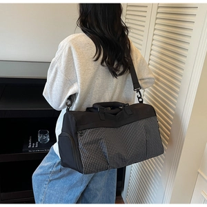 Black travel bag with gray checkered front pocket and adjustable shoulder strap detail