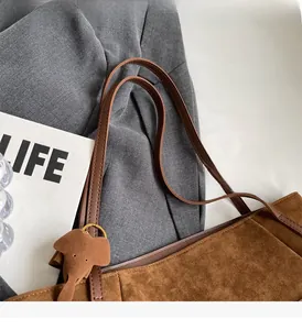 Detail shot of brown suede tote bag featuring leather handles and cute elephant charm