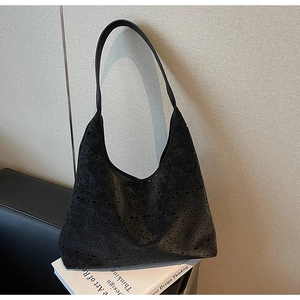 Detail of laser-cut geometric patterns on black leather tote bag with inner pouch