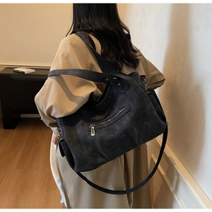 Detail of vintage black tote bag with side pocket and dual straps shown on shoulder