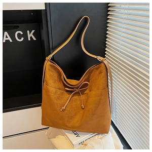 Close-up of caramel matte suede shoulder bag with thin bow detail and silver rings