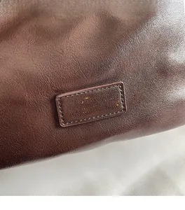 Detail of premium brown leather texture with golden embossed logo on a pleated dumpling bag