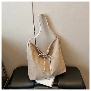 Detail view of beige tote bag with drawstring bow on a black leather bench