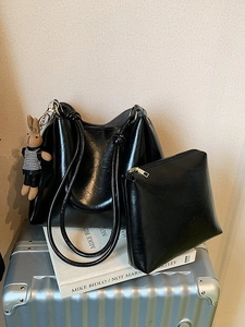 Glossy black tote bag set with bunny pendant on white book and silver suitcase
