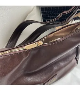 Close-up of golden metal zipper and textured dark brown leather on a luxury hobo bag