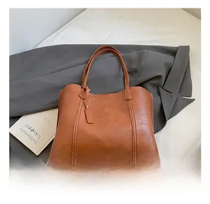 Detail of a brown leather tote bag with a rectangular tag on a stylish coat background