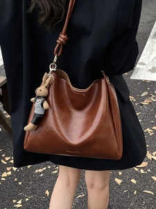 Brown vintage faux leather tote bag with rabbit charm shown on a casual street background
