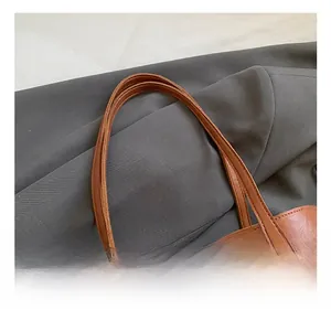 Detail of brown leather tote bag handle featuring reinforced double stitching and texture