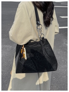 Detail of black leopard print tote bag featuring a chunky chain strap and wood bead tassel