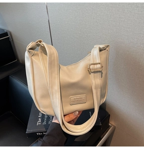 Detail view of cream white dumpling bag with brand patch and golden metal buckle hardware