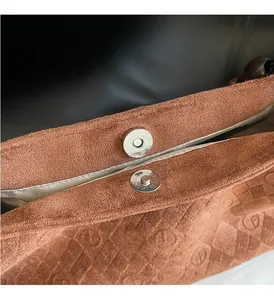 Close-up of silver magnetic buckle on brown suede bag with geometric embossed logo