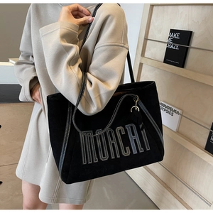 Close-up of black tote bag with white contrast stitching and tassel accessory detail