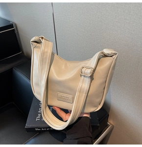 Detail of cream-white pleated dumpling bag showing PU leather texture and brand label