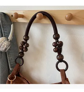 Detail of a dark brown suede handbag featuring a wooden bead and woven rope handle design