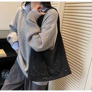 Side view of black laser-cut hollow tote bag with floral patterns on a casual model