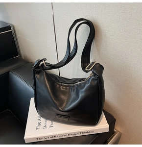 Detailed view of black lychee texture leather dumpling bag with metal zipper on a white book