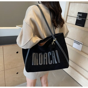 Detail of black suede tote bag with MOACHI lettering and decorative animal charm