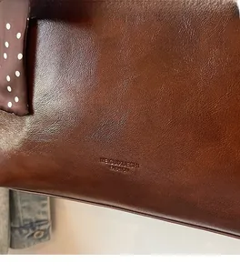 Close-up of brown textured leather tote bag with polka dot scarf and embossed logo detail