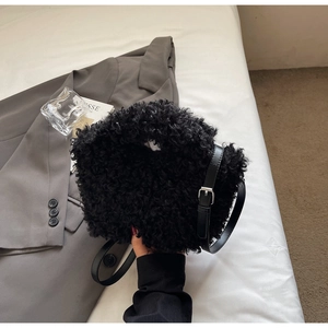 Detail of black fuzzy faux shearling handbag with leather strap and metal buckles