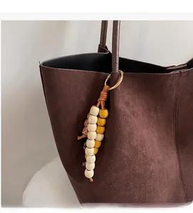 Detail of beaded bag charm with yellow and patterned beads on a brown suede tote