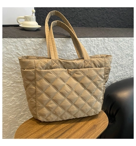 Detail of khaki quilted nylon tote bag with large diamond stitching on a wooden stool