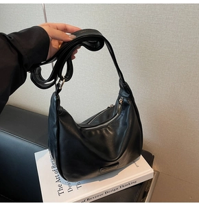 Detail of black semi-circle crossbody bag featuring adjustable strap and smooth PU texture