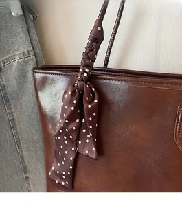 Detail of a dark brown leather tote bag handle wrapped in a brown polka dot silk scarf